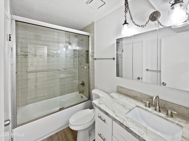 full bathroom featuring vanity, hardwood / wood-style flooring, toilet, and bath / shower combo with glass door