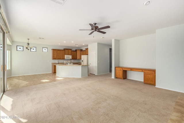 unfurnished living room featuring sink, built in desk, light colored carpet, and ceiling fan