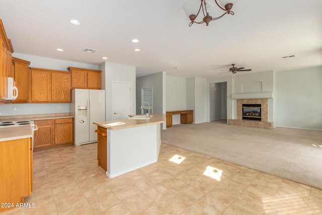 kitchen with sink, white appliances, light colored carpet, ceiling fan, and a kitchen island with sink