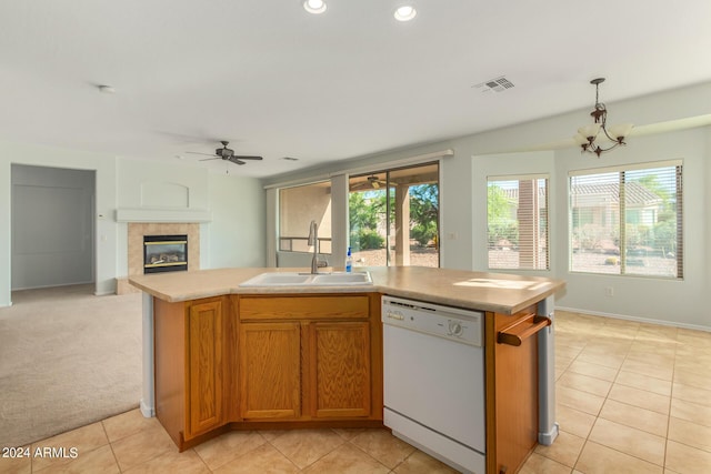 kitchen with pendant lighting, sink, dishwasher, an island with sink, and a tiled fireplace