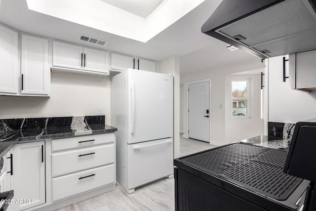 kitchen featuring white refrigerator, white cabinets, range hood, and dark stone counters