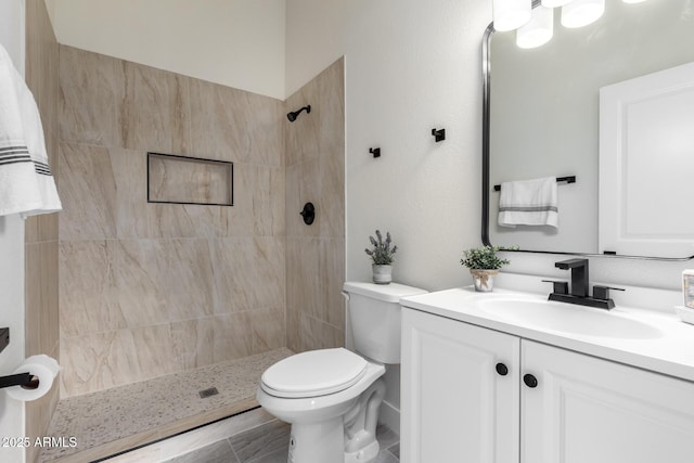 bathroom featuring tiled shower, toilet, and vanity