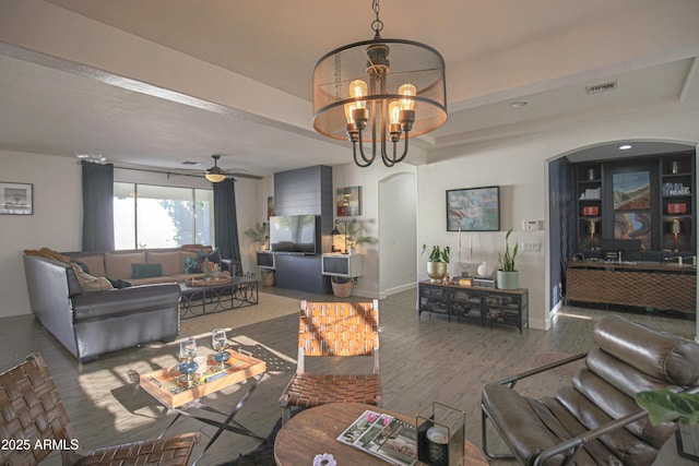 living room with a tray ceiling, hardwood / wood-style floors, ceiling fan with notable chandelier, and built in shelves