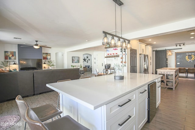 kitchen featuring decorative light fixtures, white cabinets, stainless steel fridge, a kitchen breakfast bar, and a center island