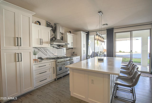 kitchen with wall chimney range hood, white cabinetry, double oven range, hanging light fixtures, and a center island