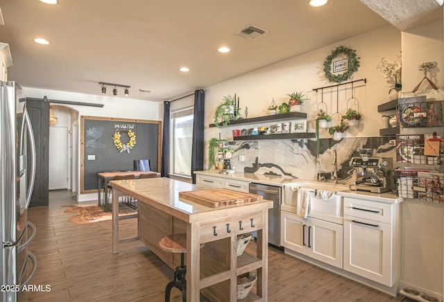 kitchen featuring a barn door, appliances with stainless steel finishes, white cabinets, and dark hardwood / wood-style flooring