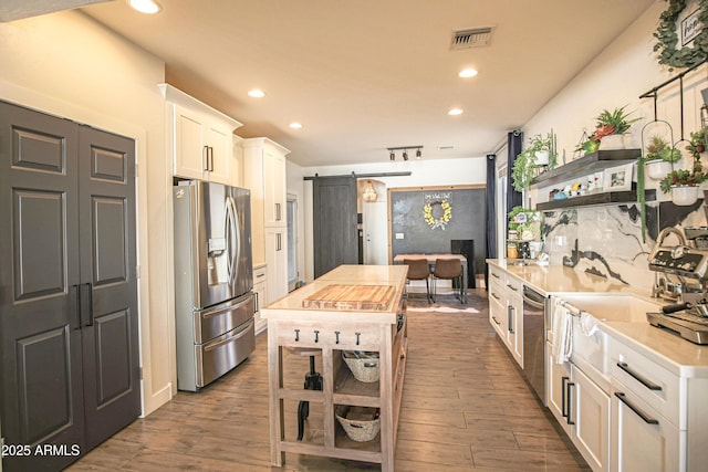 kitchen with butcher block countertops, white cabinetry, stainless steel appliances, a center island, and a barn door