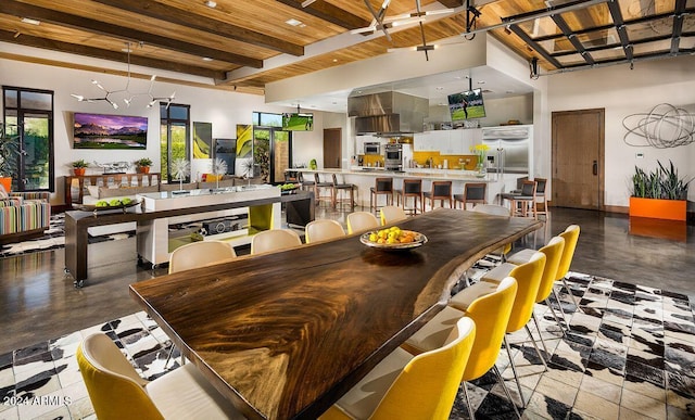 dining room featuring beam ceiling, wood ceiling, a towering ceiling, and concrete floors