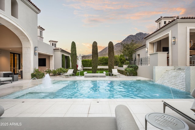 pool at dusk featuring pool water feature and a mountain view