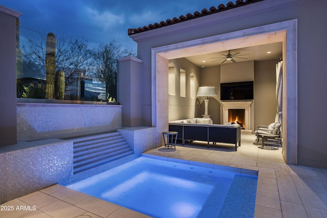 pool at dusk with a patio area and an outdoor living space with a fireplace