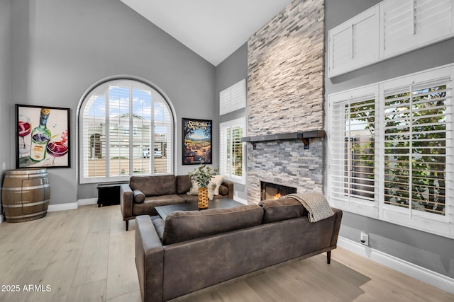 living room featuring baseboards, high vaulted ceiling, light wood-style flooring, and a fireplace