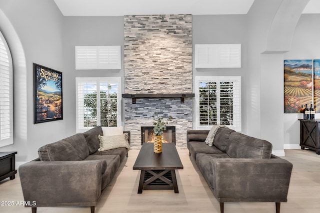 living area featuring baseboards, a stone fireplace, a high ceiling, wood finished floors, and arched walkways