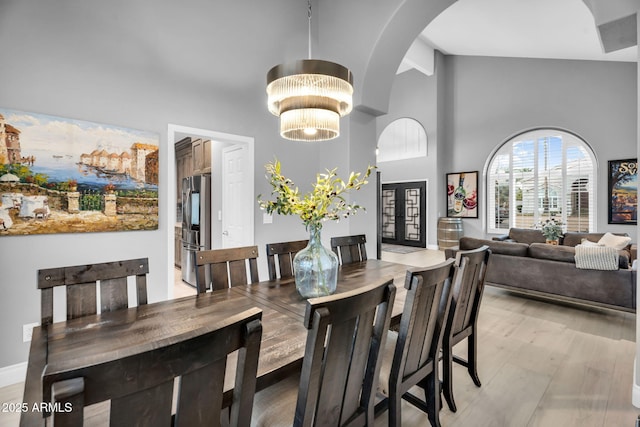 dining room with arched walkways, light wood finished floors, and high vaulted ceiling