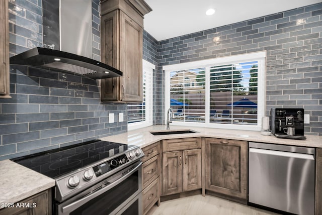 kitchen featuring a sink, backsplash, recessed lighting, stainless steel appliances, and wall chimney range hood