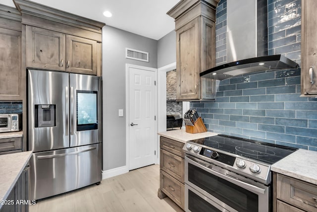 kitchen with visible vents, wall chimney range hood, decorative backsplash, appliances with stainless steel finishes, and light wood-style floors