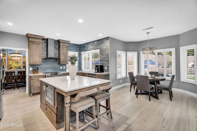 kitchen with visible vents, backsplash, appliances with stainless steel finishes, wall chimney exhaust hood, and light wood finished floors