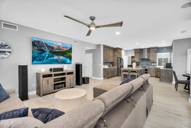 living area featuring light wood-style flooring, a ceiling fan, visible vents, and baseboards