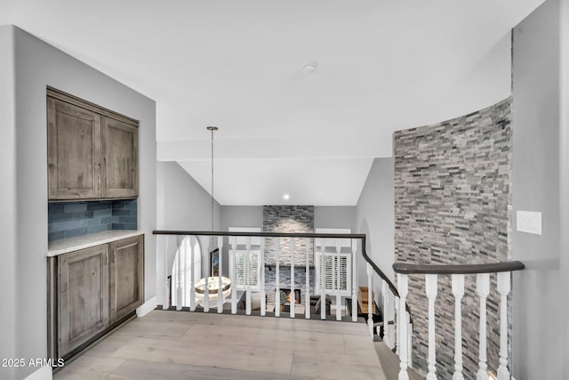 hallway featuring lofted ceiling, an upstairs landing, and light wood finished floors