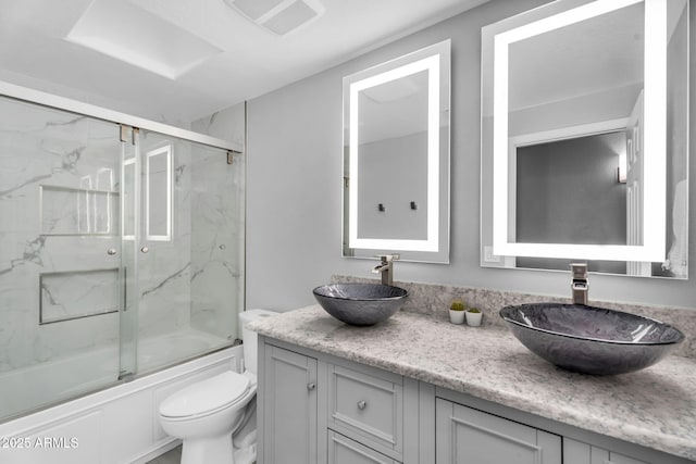 full bathroom featuring double vanity, toilet, bath / shower combo with glass door, and a sink