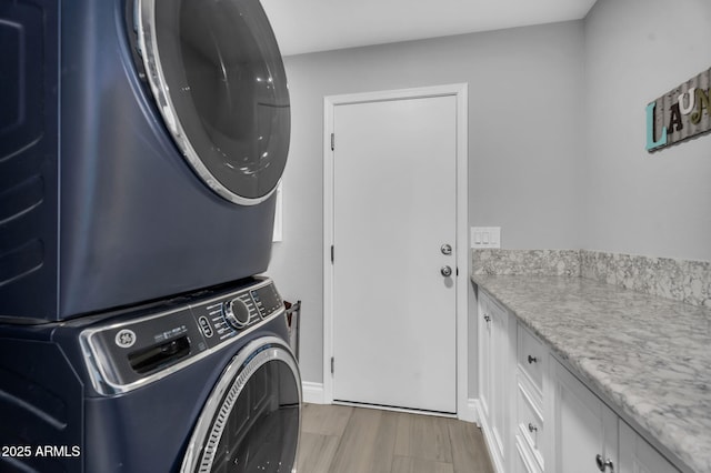 clothes washing area with light wood-type flooring, stacked washer / drying machine, and cabinet space