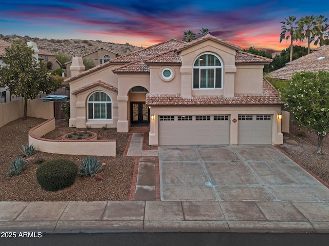 mediterranean / spanish-style home with a garage, concrete driveway, stucco siding, and a tile roof