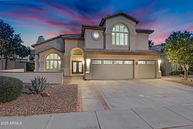 mediterranean / spanish-style house with a tile roof, stucco siding, french doors, driveway, and an attached garage