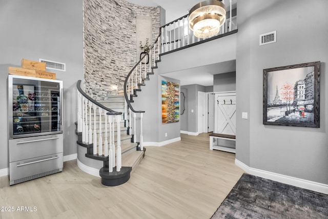 entryway featuring visible vents, wood finished floors, wine cooler, a high ceiling, and baseboards