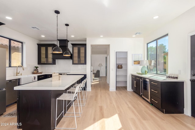 kitchen featuring pendant lighting, sink, light hardwood / wood-style flooring, a kitchen island, and custom exhaust hood