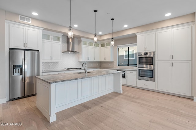 kitchen with a kitchen island with sink, wall chimney exhaust hood, light stone counters, white cabinetry, and stainless steel appliances