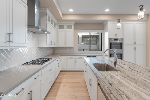 kitchen featuring white cabinetry, sink, wall chimney exhaust hood, pendant lighting, and appliances with stainless steel finishes