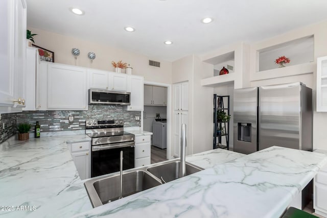 kitchen with white cabinetry, backsplash, washer and dryer, stainless steel appliances, and light stone counters