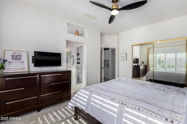 bedroom with ceiling fan, light colored carpet, a closet, and ensuite bath