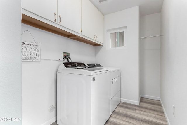 clothes washing area featuring cabinets, washing machine and dryer, and light hardwood / wood-style floors