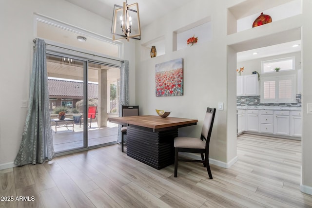 dining space with an inviting chandelier, a towering ceiling, and light wood-type flooring