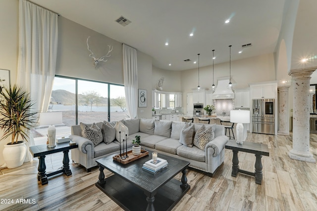 living room featuring ornate columns, a towering ceiling, light hardwood / wood-style flooring, and a water and mountain view