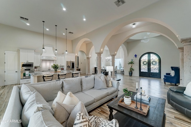 living room with decorative columns, a notable chandelier, light wood-type flooring, and french doors