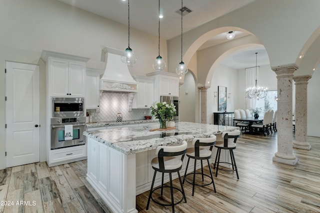 kitchen with a large island, white cabinets, light stone counters, and light wood-type flooring