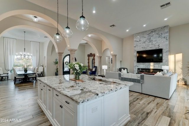 kitchen with light wood-type flooring, a fireplace, pendant lighting, white cabinets, and a center island with sink