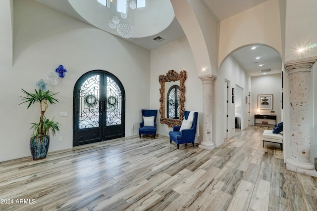 foyer with french doors, ornate columns, light wood-type flooring, and a towering ceiling