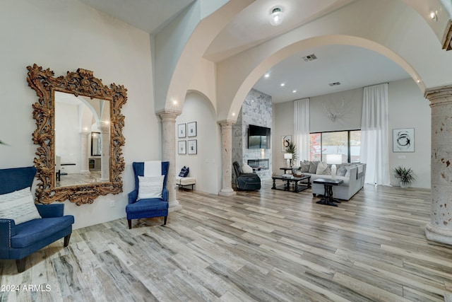 sitting room featuring a high ceiling, ornate columns, and light wood-type flooring