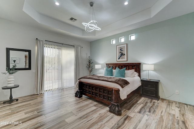 bedroom featuring light hardwood / wood-style floors, multiple windows, and a tray ceiling