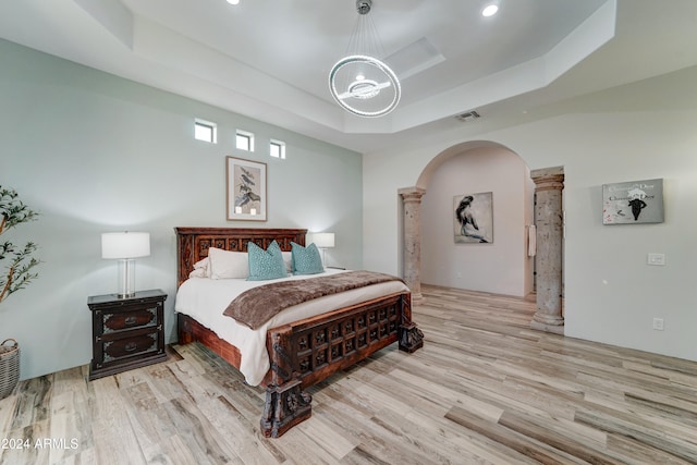 bedroom featuring light hardwood / wood-style floors, a raised ceiling, and decorative columns