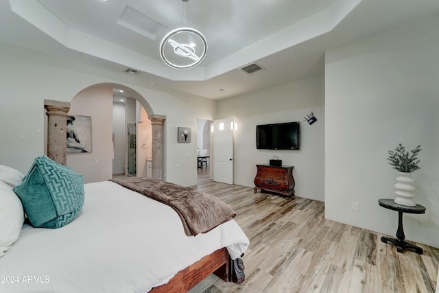 bedroom with light hardwood / wood-style floors, a chandelier, ornate columns, and a raised ceiling