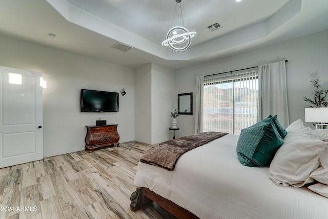 bedroom with a raised ceiling, access to outside, an inviting chandelier, and light wood-type flooring