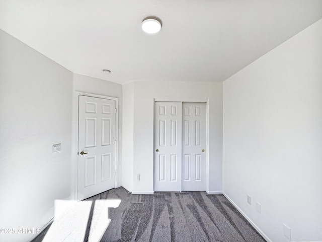 unfurnished bedroom with dark colored carpet and a closet