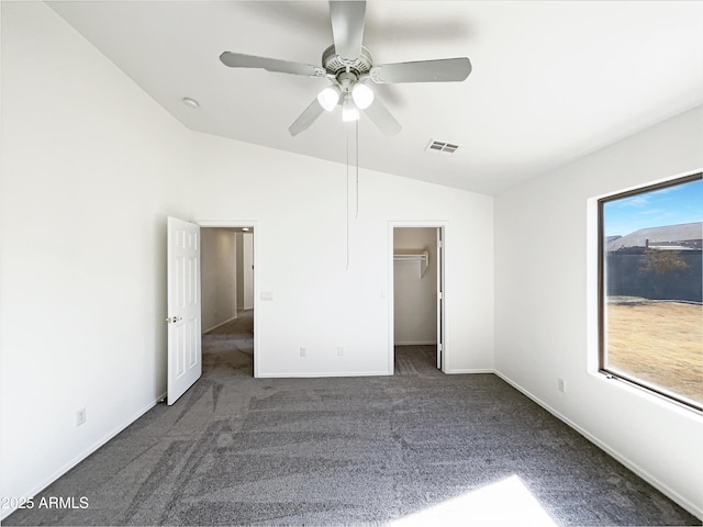 unfurnished bedroom with dark carpet, ceiling fan, a spacious closet, a closet, and lofted ceiling