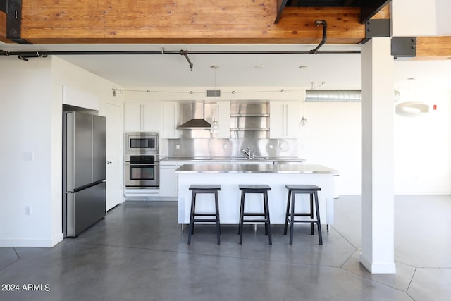 kitchen featuring appliances with stainless steel finishes, stainless steel counters, white cabinets, a breakfast bar area, and wall chimney range hood