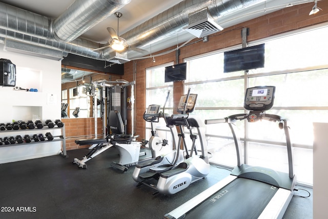 exercise room featuring ceiling fan and brick wall