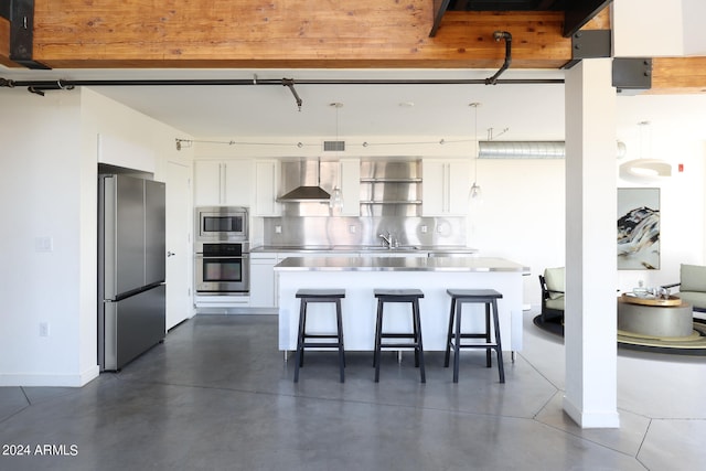 kitchen featuring appliances with stainless steel finishes, white cabinetry, stainless steel counters, wall chimney exhaust hood, and a breakfast bar area