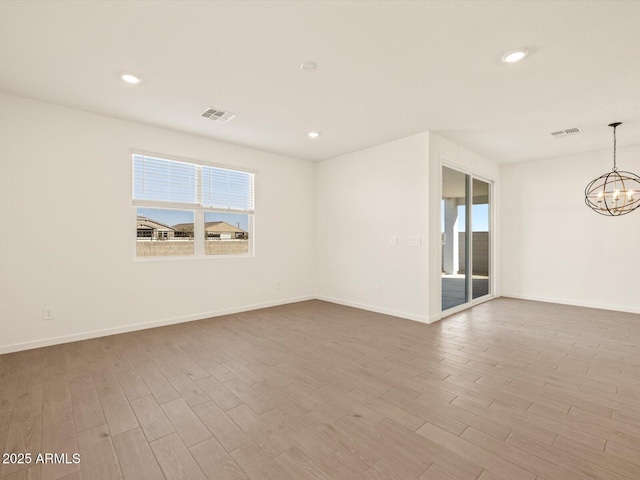 spare room with a healthy amount of sunlight, light hardwood / wood-style flooring, and a chandelier